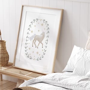 Framed unicorn wall art leaning on a wooden bench beside white bedding and a woven basket in a soft-lit bedroom.
