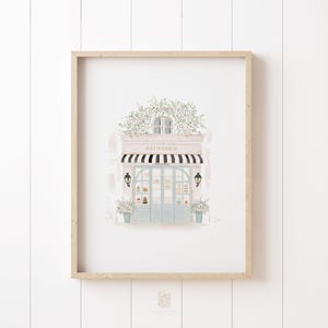 Soft watercolor illustration of a French patisserie storefront with a black-and-white striped awning, potted plants, and delicate floral details. A charming printable art piece for Paris lovers.