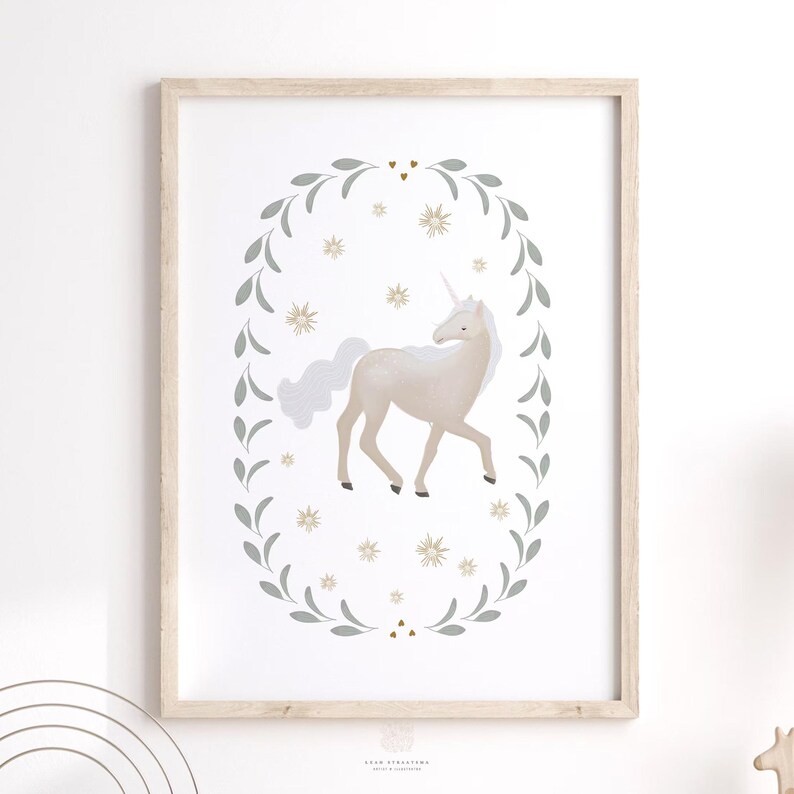 Neutral unicorn print framed in light wood and hung on a white wall with soft shadowing, in a kids playroom.