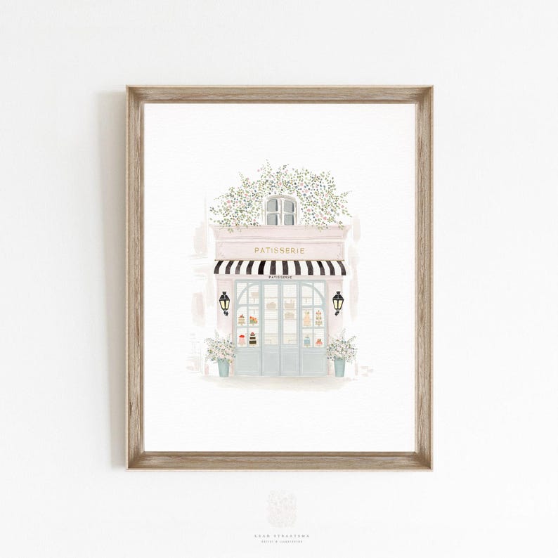 French bakery art print in a light wood frame, soft watercolor illustration of a Paris cafe storefront in neutral pastel tones.