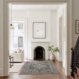 Vintage swan artwork displayed above a black fireplace at the end of a bright hallway, with white walls, wood floors, a patterned runner rug and a large ceramic vase nearby.
