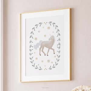 Unicorn nursery artwork in white and gold frame, mounted on a pale pink wall with simple clean surroundings.