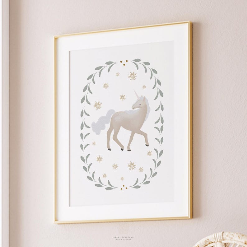 Unicorn nursery artwork in white and gold frame, mounted on a pale pink wall with simple clean surroundings.