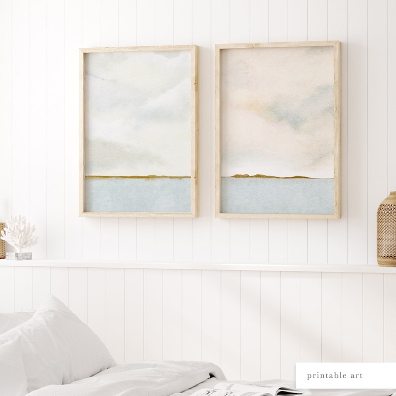 A pair of minimalist ocean horizon prints with delicate gold-green toned detailing, hung on a bedroom wall for effortless styling.