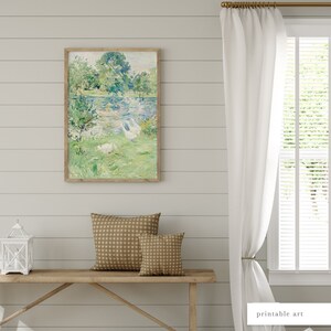 Puede incluir: Una pintura enmarcada que representa una escena de paisaje con un lago, &aacute;rboles y p&aacute;jaros blancos. La pintura est&aacute; colgada en una pared blanca con paneles de madera. Hay un banco de madera con dos cojines marrones delante de la pintura.