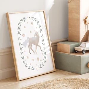Unicorn print leaning in a natural wood frame, styled on floor next to stacked toy boxes and a wooden wand.