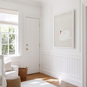 Framed white swan painting hanging on a paneled wall in a sunlit nursery, showing the bird in profile against a soft cream background.