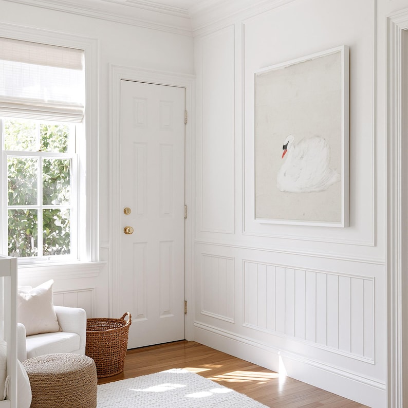 Framed white swan painting hanging on a paneled wall in a sunlit nursery, showing the bird in profile against a soft cream background.