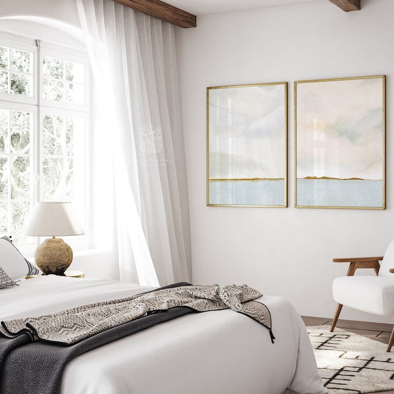 Soft coastal abstract prints framed in light wood, featuring neutral tones of blue, beige, and white, styled in a serene bedroom setting.