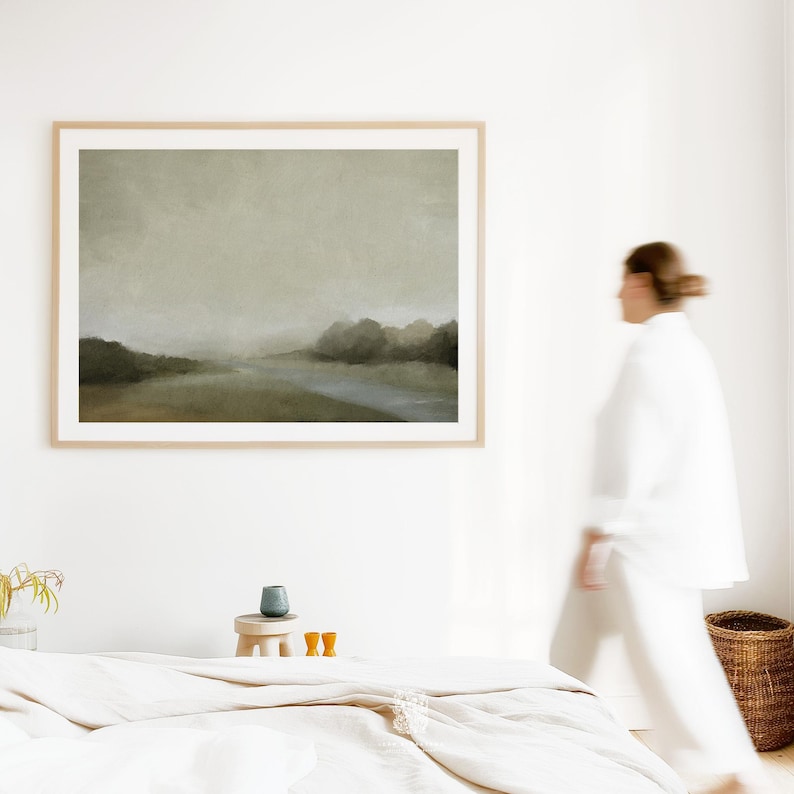 Framed moody landscape wall art featuring a soft forest scene with muted greens and a peaceful grey sky, styled above a neutral bed in a serene bedroom.