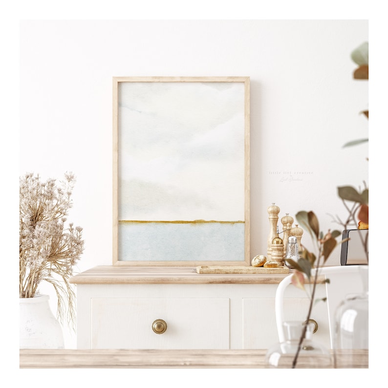 Elegant watercolour painting of a coastal horizon. The artwork showcases soft blue-grey skies merging with a serene blue sea, accented by a thin golden green shoreline, capturing a sense of calm and simplicity.