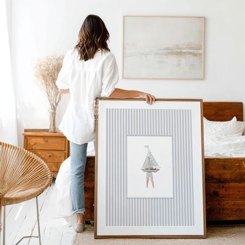 Large sailboat wall print held at the end of a bed in a neutral bedroom, showing scale and styling for a coastal or lakehouse kids room.