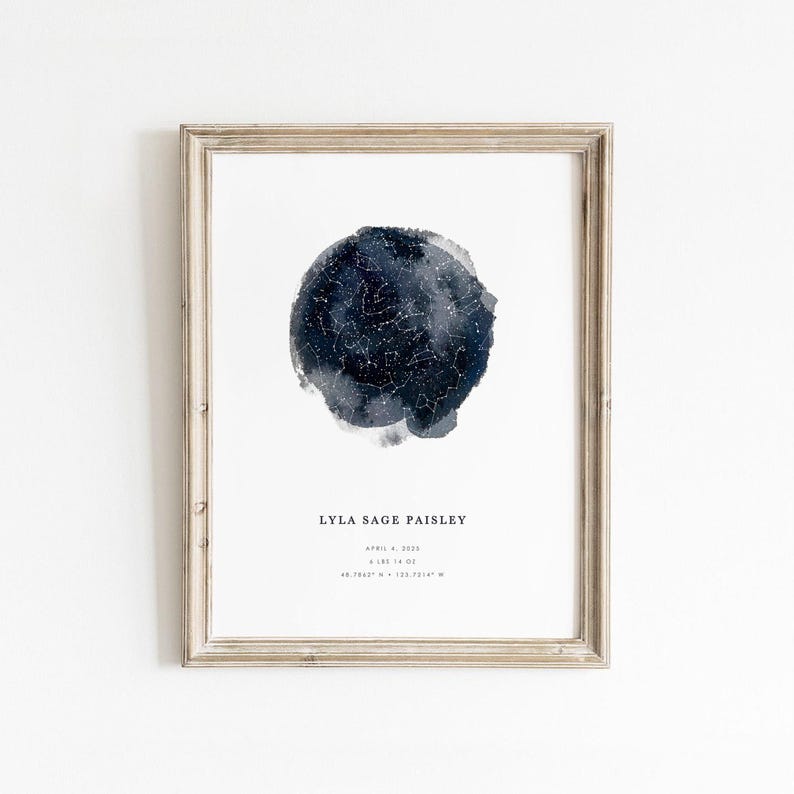 A personalized watercolour star map print in a rustic light wood frame, showing a navy and grey night sky filled with white constellations. Below it, a baby's name, birth date, weight, and coordinates, with a calm, minimalist nursery feel.