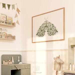 Green botanical moth print in a thin wood frame displayed in a child’s room, with floral patterned wings above a sage green play kitchen and wooden rocking horse.