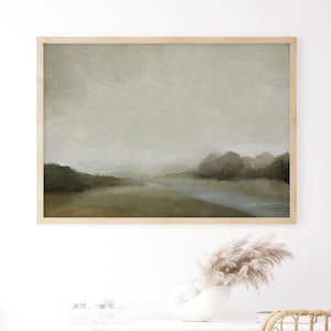 Framed moody forest landscape print with soft trees, muted green tones, and a calm sky, styled as bedroom wall decor in a neutral space.