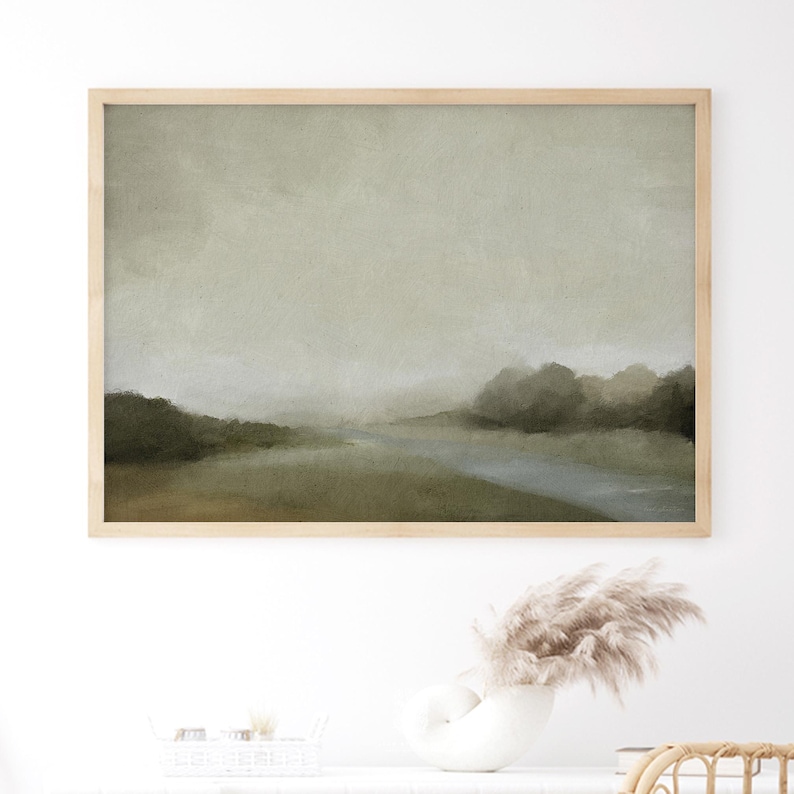 Framed moody forest landscape print with soft trees, muted green tones, and a calm sky, styled as bedroom wall decor in a neutral space.