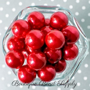 May include: A bowl filled with bright red round beads. The beads are shiny and have a pearlescent finish.