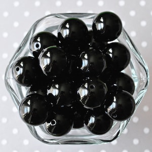 May include: A clear glass bowl filled with glossy, black, round beads. The beads have a smooth, reflective surface and are evenly spaced within the bowl. The bowl has a unique, multi-sided shape.