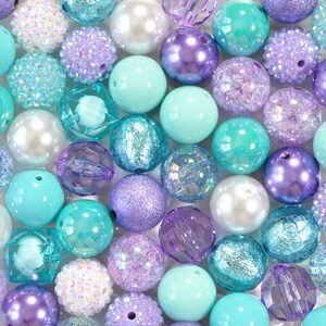May include: An assortment of colorful beads in shades of turquoise, lavender, and white. The beads vary in texture, including smooth, glittery, and faceted designs. Some beads have a pearl-like sheen, while others are opaque.