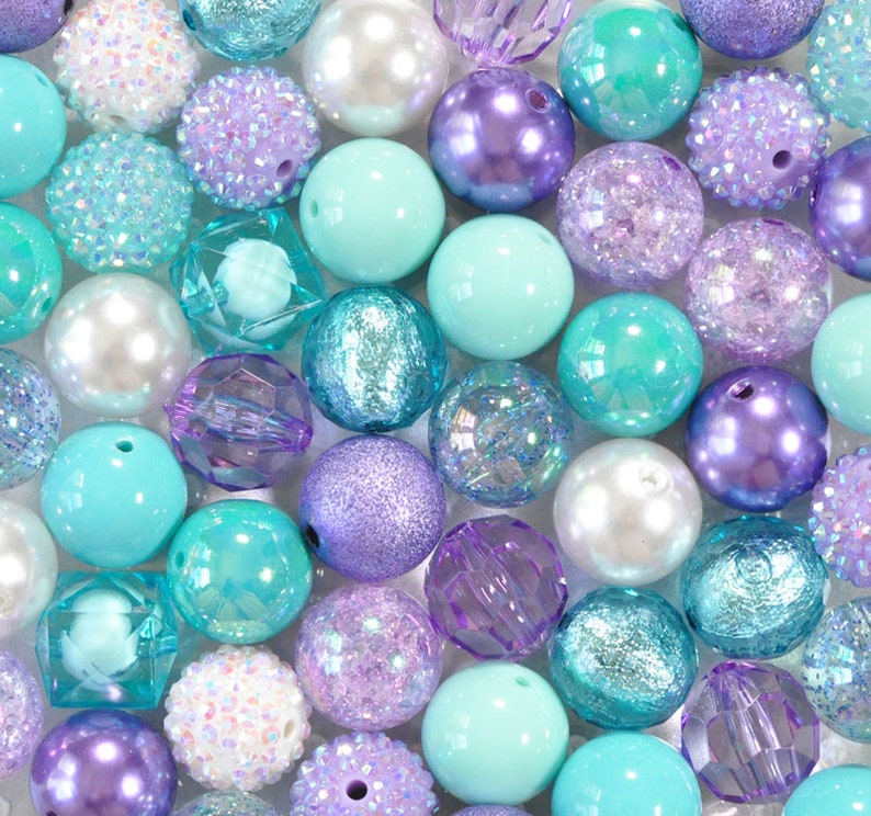 May include: An assortment of colorful beads in shades of turquoise, lavender, and white. The beads vary in texture, including smooth, glittery, and faceted designs. Some beads have a pearl-like sheen, while others are opaque.