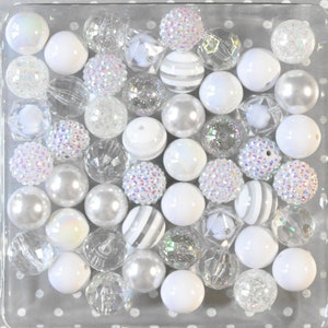 May include: A collection of white and silver beads in a clear glass container. The beads are various shapes and sizes, including round, square, and star-shaped. Some beads have a sparkly finish.