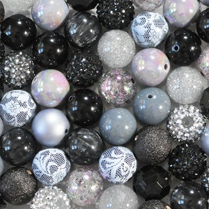 May include: A collection of black, white and silver beads. The beads are made from a variety of materials, including glass, plastic and metal. Some of the beads have a sparkly finish, while others have a matte finish.