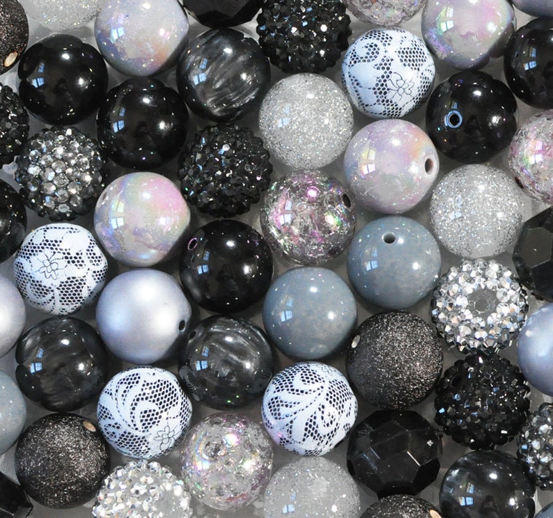 May include: A collection of black, white and silver beads. The beads are made from a variety of materials, including glass, plastic and metal. Some of the beads have a sparkly finish, while others have a matte finish.
