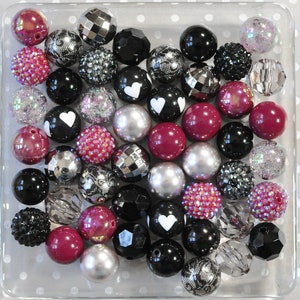 May include: A collection of colorful beads in various shapes and sizes, including hearts, swirls, and geometric patterns. The beads are primarily black, white, and pink with some silver and clear accents.