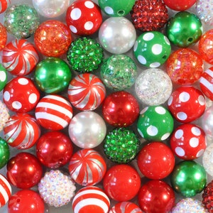 May include: A collection of colorful beads in various sizes and textures. The beads are primarily red, green, and white, with some featuring polka dots, stripes, or glitter. Some beads are solid, while others have a pearlescent or textured finish. The beads are arranged closely together.