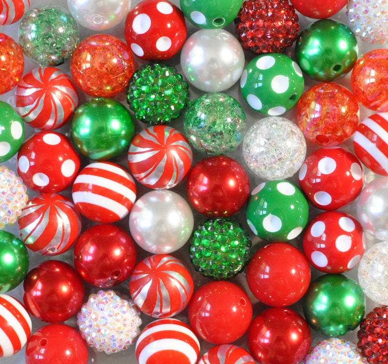 May include: A collection of colorful beads in various sizes and textures. The beads are primarily red, green, and white, with some featuring polka dots, stripes, or glitter. Some beads are solid, while others have a pearlescent or textured finish. The beads are arranged closely together.