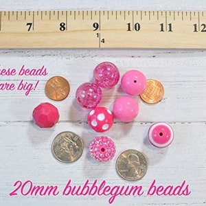 May include: A collection of 20mm bubblegum pink beads in various styles, including solid, speckled, and polka dot. The beads are shown next to UK currency for size comparison. "These beads are big!" is written in white text on a black background.