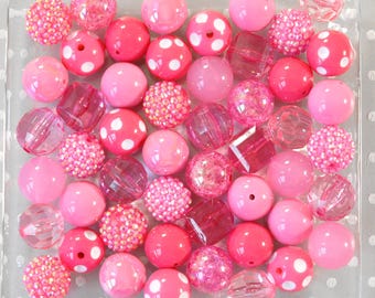 Könnte beinhalten: Eine Sammlung rosa Perlen in verschiedenen Farbtönen und Stilen. Einige Perlen sind einfarbig, andere haben weiße Tupfen, und einige sind mit kleinen, glitzernden Verzierungen bedeckt. Es gibt auch facettierte und klare Perlen. Die Perlen sind in einem transparenten, quadratischen Behälter angeordnet.