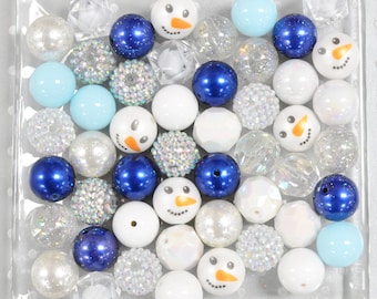 Könnte beinhalten: Eine Sammlung verschiedener Perlen in einer transparenten Schale. Die Perlen sind weiß, blau und klar, einige mit Schneemann-Gesichtern. Verschiedene Perlenarten, darunter Glitzer-, facettierte und perlmuttartige Oberflächen. Ideal für Schmuckherstellung oder Bastelprojekte.