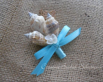 May include: A small bouquet of seashells tied together with a light blue ribbon. The bouquet is decorated with a white seashell and a pearl. The bouquet is sitting on a burlap background. Creative Bridal Solutions Aqua.