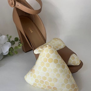 May include: A pair of tan heeled sandals with a buckle strap. The sandals are sitting on a white surface with a yellow and white honeycomb patterned fabric shoe insert.