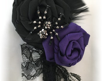 May include: A black and purple fabric flower with a black spider and rhinestones, accented with black lace and a black feather.