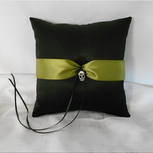 May include: A black pillow with a green satin ribbon and a silver skull accent. The pillow is on a white surface.