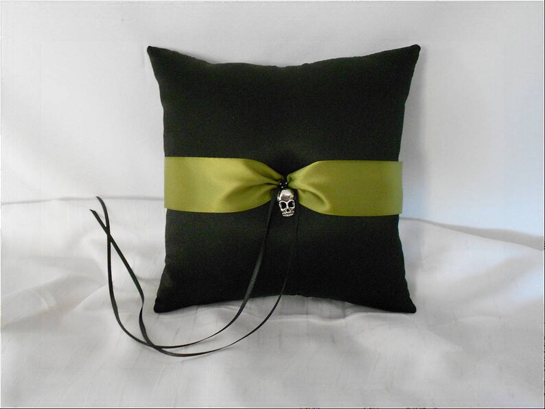 May include: A black pillow with a green satin ribbon and a silver skull accent. The pillow is on a white surface.