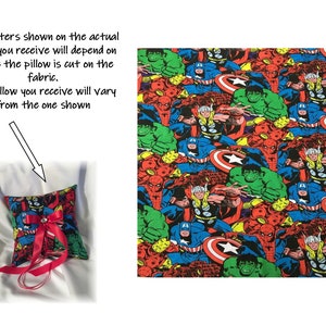 May include: A red and white ring pillow with a superhero fabric design. The fabric features a repeating pattern of various superheroes, including Spider-Man, Hulk, Captain America, and Thor. The pillow is decorated with a red satin ribbon and a single rhinestone.
