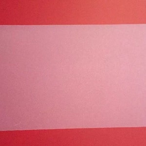 May include: A rectangular, translucent, pink plastic sheet with rounded corners. The sheet is set against a red background. The surface of the sheet has a slightly textured appearance.