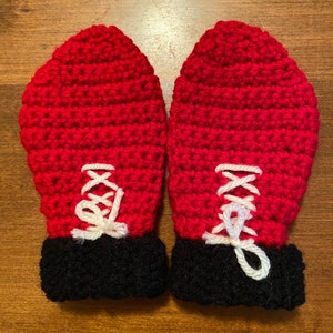 Peut inclure: Une paire de mitaines en crochet rouge avec des poignets noirs et des lacets en crochet blanc.