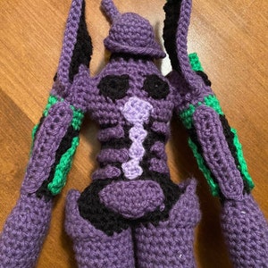 May include: Crocheted purple and green amigurumi figure of a robot with a black and purple design.