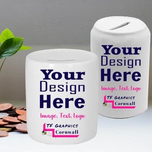 Può includere: Due salvadanai in ceramica bianca con uno slot nella parte superiore. Entrambi i salvadanai hanno il testo "Your Design Here" in lettere blu e il testo "Image, Text, Logo" in lettere nere. La parte inferiore di ogni salvadanaio ha una grafica rosa e nera con il testo "TF Graphics Cornwall".