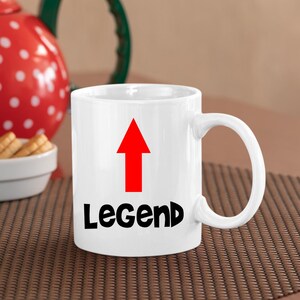 May include: White ceramic mug with a red arrow pointing upwards and the word "Legend" in black lettering.