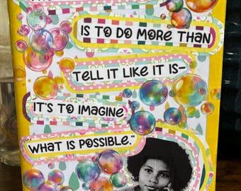 Könnte beinhalten: Ein gelber Notizbuchumschlag mit einer Collage aus bunten Seifenblasen und einem schwarz-weißen Porträt von bell hooks. Der Text lautet: The function of art is to do more than tell it like it is—it's to imagine what is possible. — bell hooks.