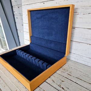 May include: A wooden box with a blue velvet interior and slots for holding silverware. The box is open and the lid is propped up.