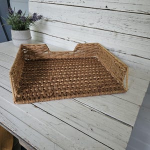 May include: A rectangular woven wicker desk tray with a natural light brown finish. The tray features a flat base with a grid-like weave pattern and raised sides, including a lower front section for easy access to documents or papers.