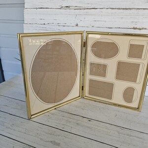 May include: A gold-toned, hinged picture frame with multiple openings. One side features a large oval opening, while the other has a variety of smaller rectangular and oval openings. The frame is set against a neutral background.