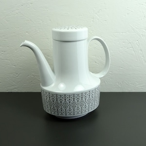 Op de afbeelding: Witte koffiekan van keramiek met een geometrisch patroon in zwart en wit. De kan heeft een tuit en een handvat.