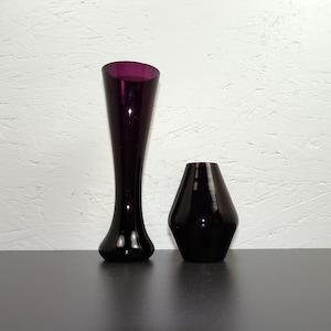 Könnte beinhalten: Zwei violette Glasvasen, eine hoch und schlank, die andere kürzer und breiter, beide mit glänzender Oberfläche.